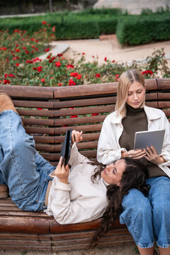 Two women using tablet and smartphone on park bench