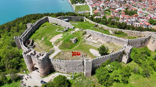 Aerial drone view of Tsar Samuel's Fortress on a hill in Ohrid, North Macedonia, with the national flag waving in the wind. Scenic panorama overlooking Lake Ohrid and the surrounding landscape. 