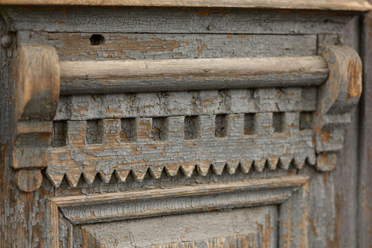 Detailed close-up of an aged carved wooden panel featuring geometric dentil molding, rounded horizontal rail, and layered rectangular trim. Surface shows