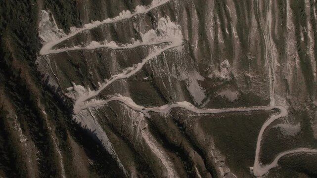 Drone footage of the steep serpentine road descending Katu-Yaryk Pass above a rugged canyon and taiga forest in the Altai Mountains, Russia, sunny day