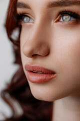 Fototapeta premium Detailed close-up of a womans face with soft natural makeup, clear blue eyes, defined lips, and smooth skin against a blurred neutral background with gentle