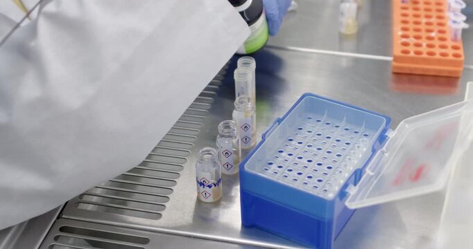 A scientist adds solvent to glass vials with signs in triangles, preparing buffers for dilution.