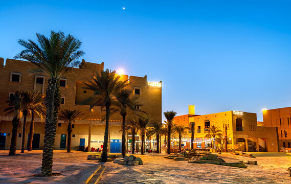 Traditional Najdi style buildings and palm trees at Souk Al Zal square illuminated at night in Riyadh, Saudi Arabia.