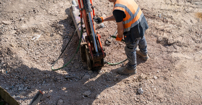 Construction worker in orange vest operating drilling machine on rocky ground
