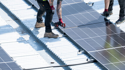 Multiple worker using drill to fasten solar panel row on bright rooftop © Preethiloki