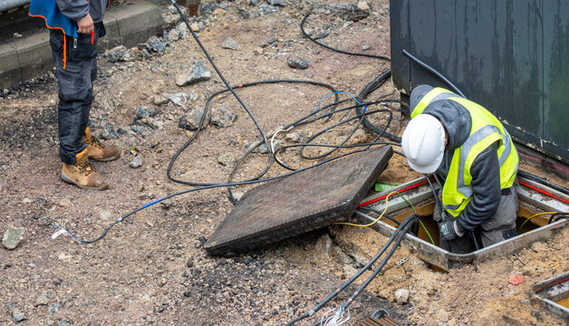 Construction worker in yellow vest working inside underground utility pit with cable and wire