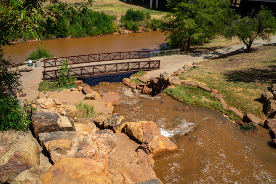 Waterfall On Red Brick and Red Rocks FLowing Under Bridge and Into River in Green Nature Park in Wichita Falls, Texas