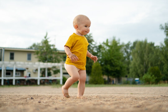 Carefree toddler walking barefoot on warm sand outdoors with playful happy steps. Child exploring ground freely on soft surface. Innocent baby discovering sandy texture under bare feet on sunny day
