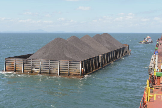 coal loaded barge approaching alongside bulk carrier vessel with tugboat assistance during offshore cargo transfer operations