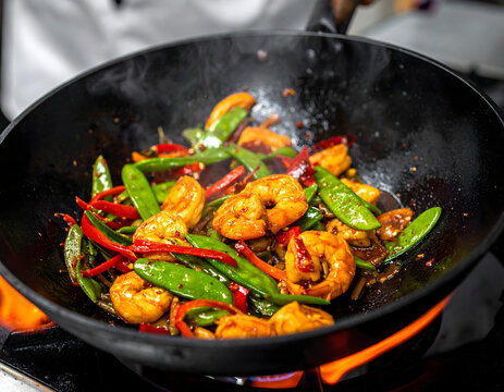 Salteado de camarones y vegetales en wok con fuego en cocina profesional