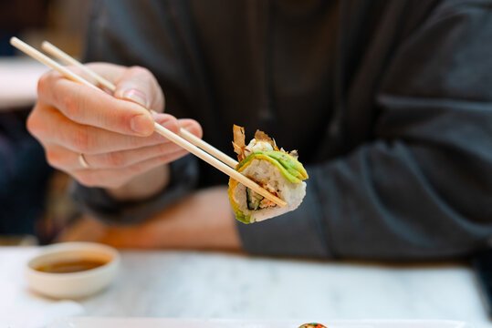A man enjoying sushi with chopsticks at a white marble restaurant table. The soy sauce bowl completes the authentic setup. He savors each piece in a peaceful atmosphere embracing simple pleasure