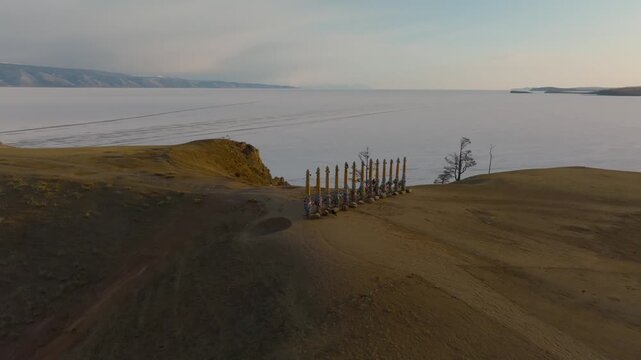 Drone footage of sacred Shaman Rock area with ritual poles on a windswept cape above the frozen shoreline of Lake Baikal, Olkhon Island, Irkutsk Oblast, Russia