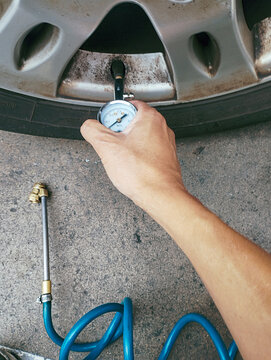 Close-up of a hand holding a tire pressure gauge. The gauge is round and silver, with a white dial displaying the readings in MPa.