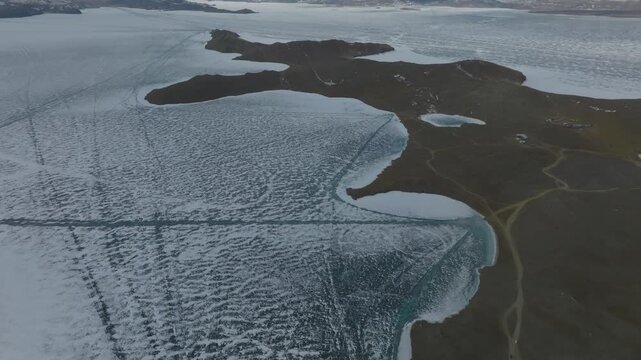 Drone footage of Cape Kobylya Golova on Olkhon Island with frozen Lake Baikal ice, cracks and snow patterns along the shoreline, Irkutsk Oblast, Russia