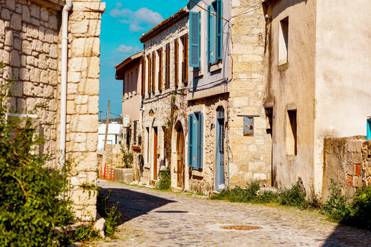 Sunlit cobblestone street with stone houses and shutters