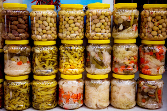 Jars of assorted pickles and olives stacked in market stall