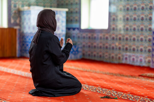 Muslim woman praying inside mosque on red carpet