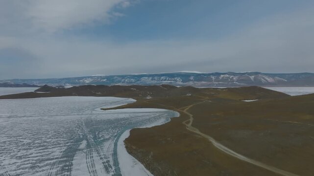 Wide aerial landscape of Kobylya Golova Cape on Olkhon Island, Lake Baikal, Russia, showing rugged shoreline, frozen water edges, hills and remote roads