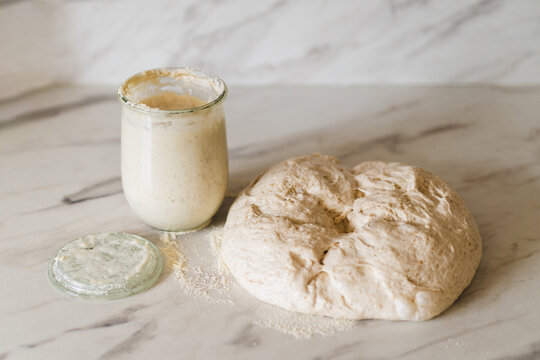 Fresh sourdough dough beside a jar of starter on marble