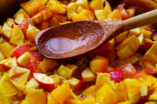 Wooden spoon with syrup in pieces of oranges and apples in jam. Selective focus.