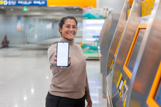Woman with phone at modern subway station ticket kiosk