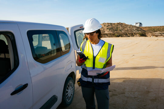 Female construction worker using smartphone by work van