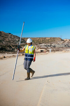 Woman construction worker surveying site with measuring rod
