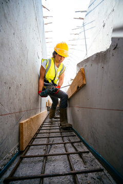 Female construction worker using power drill in concrete trench