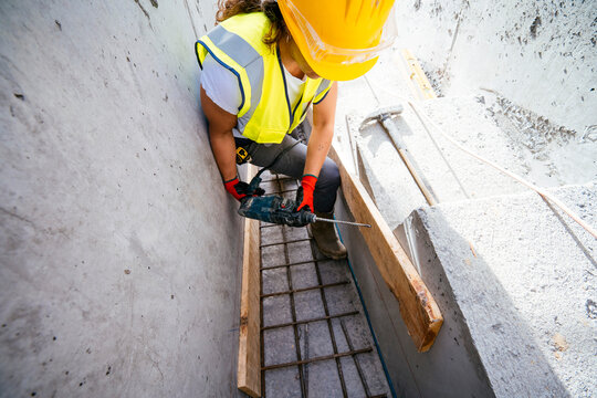 Female construction worker drilling in concrete trench on site