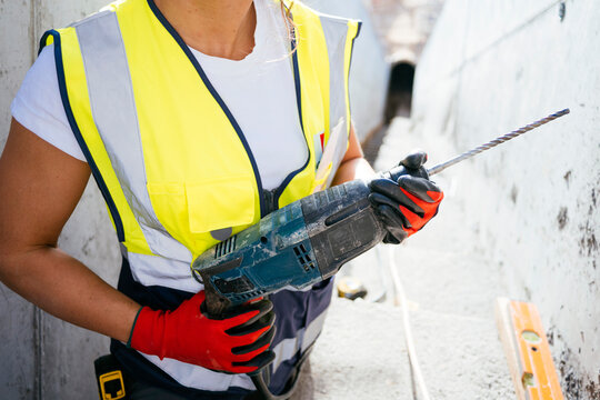 Female construction worker holding drill in safety vest
