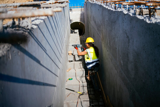 Woman construction worker drilling concrete in trench site