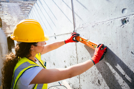 Female construction worker measuring concrete wall with level