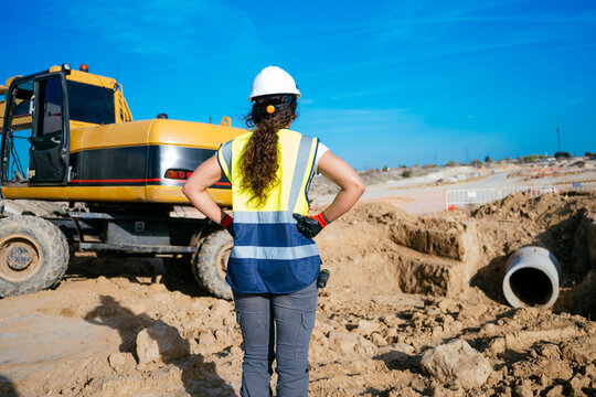 Woman construction worker supervising excavator and trench