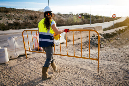 Woman construction worker carrying barrier at roadwork site