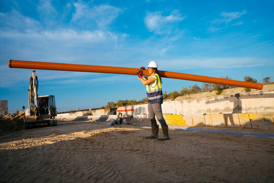 Female construction worker carrying long pipe on job site