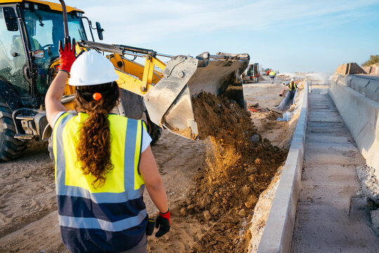 Female construction worker directing excavator at road site