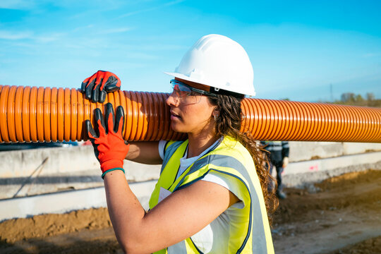 Female construction worker carrying conduit pipe at site