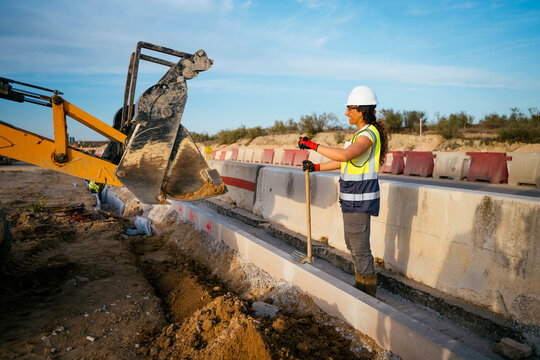 Woman construction worker in helmet guiding excavator bucket