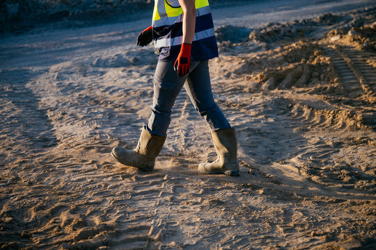 Construction worker walking on sandy site wearing safety gear