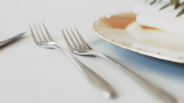 Elegant dining table setting with forks beside a white plate and soft napkin