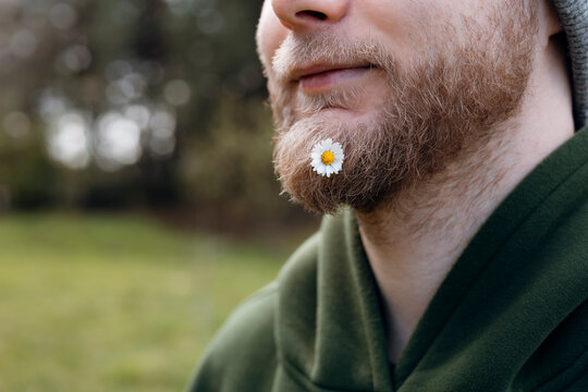 Close-up of bearded man with daisy in forest light