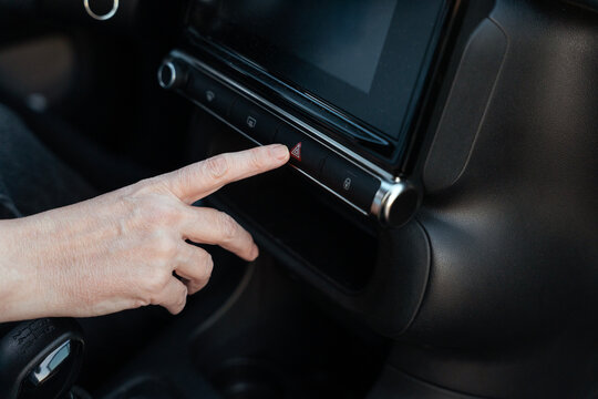 Finger pressing hazard warning button on modern car dashboard