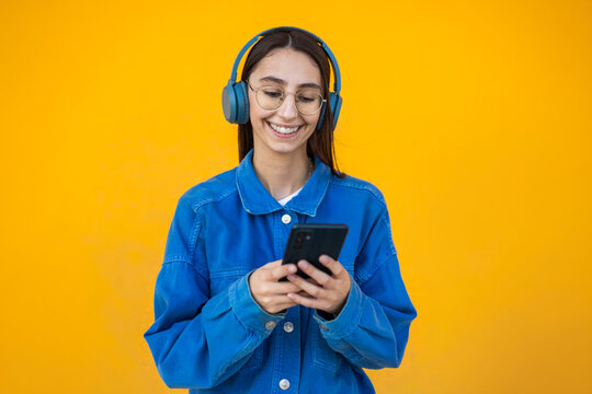 Young woman using smartphone with headphones on colorful wall
