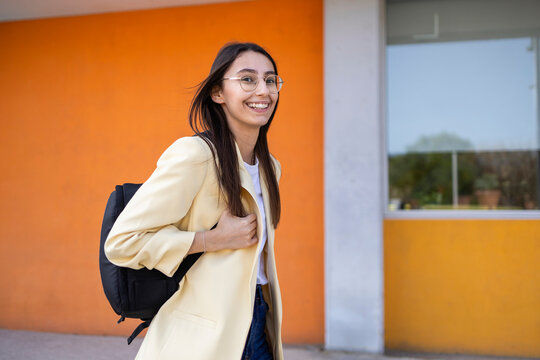 Young woman with backpack smiling against colorful wall
