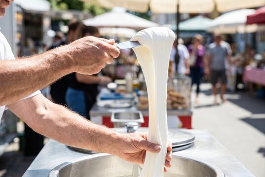 Street food vendor stretching a large thick ribbon of sweet white taffy candy at an outdoor market