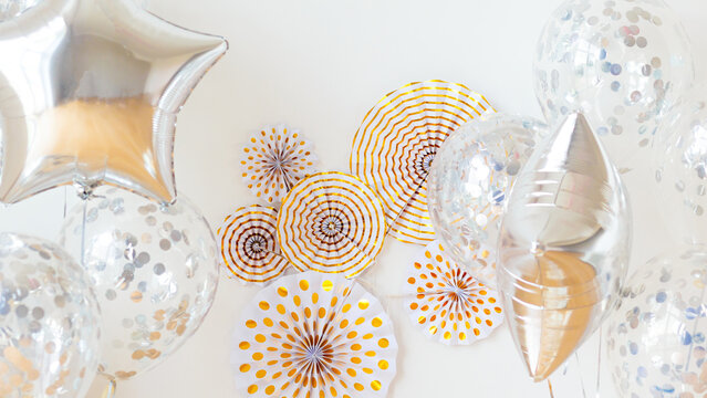 Festive silver balloons and gold paper fans on white