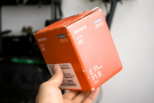 Zapopan Jalisco, Mexico - June 6, 2026: Hand holding used orange box of a Sony E 11mm f1.8 SEL11F18 lens, product box concept