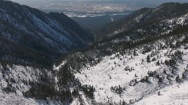 Drone footage of a snow-covered mountain valley and taiga forest near Galina Peak above Arshan, Republic of Buryatia, Russia, with distant plains on the horizon