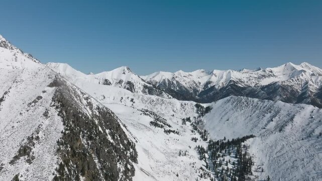 Aerial footage of snow-covered ridges and alpine valley with sparse conifer forest near Peak Galina, Arshan, Republic of Buryatia, Russia on a clear winter day