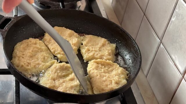 Frying crispy potato pancakes in hot oil and flipping draniki with spatula on frying pan